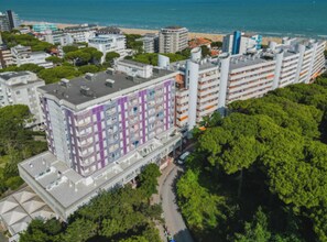 A multi-story hotel with a distinctive purple and white facade, located near a beach with a clear view of the sea. - Stylish Flat for a Perfect Getaway (Lignano Sabbiadoro)