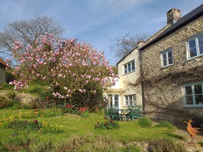 A stone building with a garden, a tree with pink flowers, and a statue of a rooster.