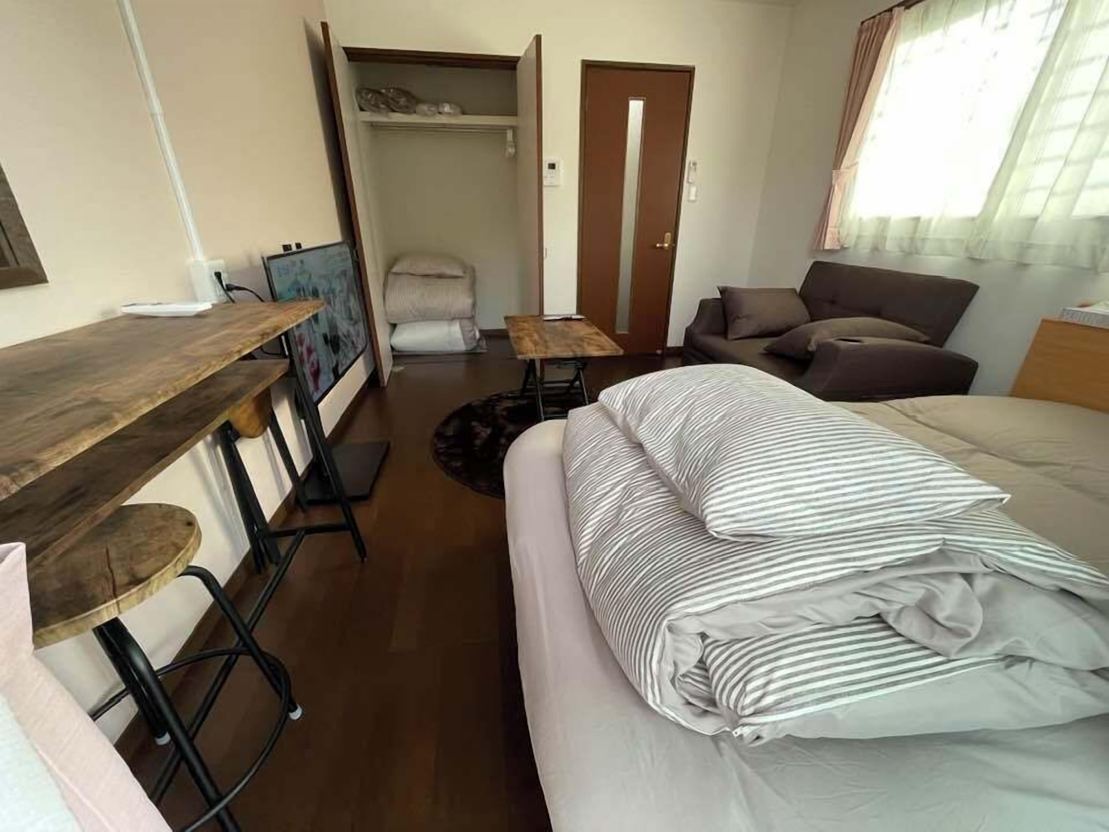 A compact room with a bed, a small table, a chair, a wardrobe, and a window.