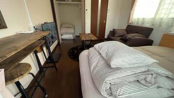 A compact room with a bed, a small table, a chair, a wardrobe, and a window.