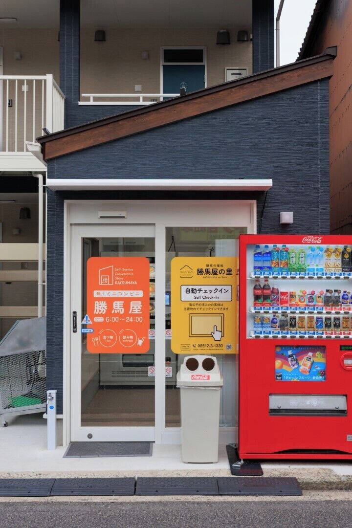 Un edificio con una máquina expendedora de Coca-Cola, un quiosco de registro propio y un cartel que indica el horario de atención.
