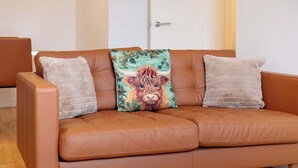 Un canapé en cuir marron avec deux coussins, l’un orné d’un motif floral et l’autre uni.