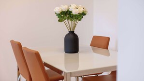 Une table à manger ornée d’un vase de fleurs blanches, entourée de chaises.