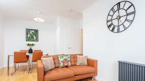 Un salon avec un canapé, des fauteuils, une table, une horloge et un radiateur.