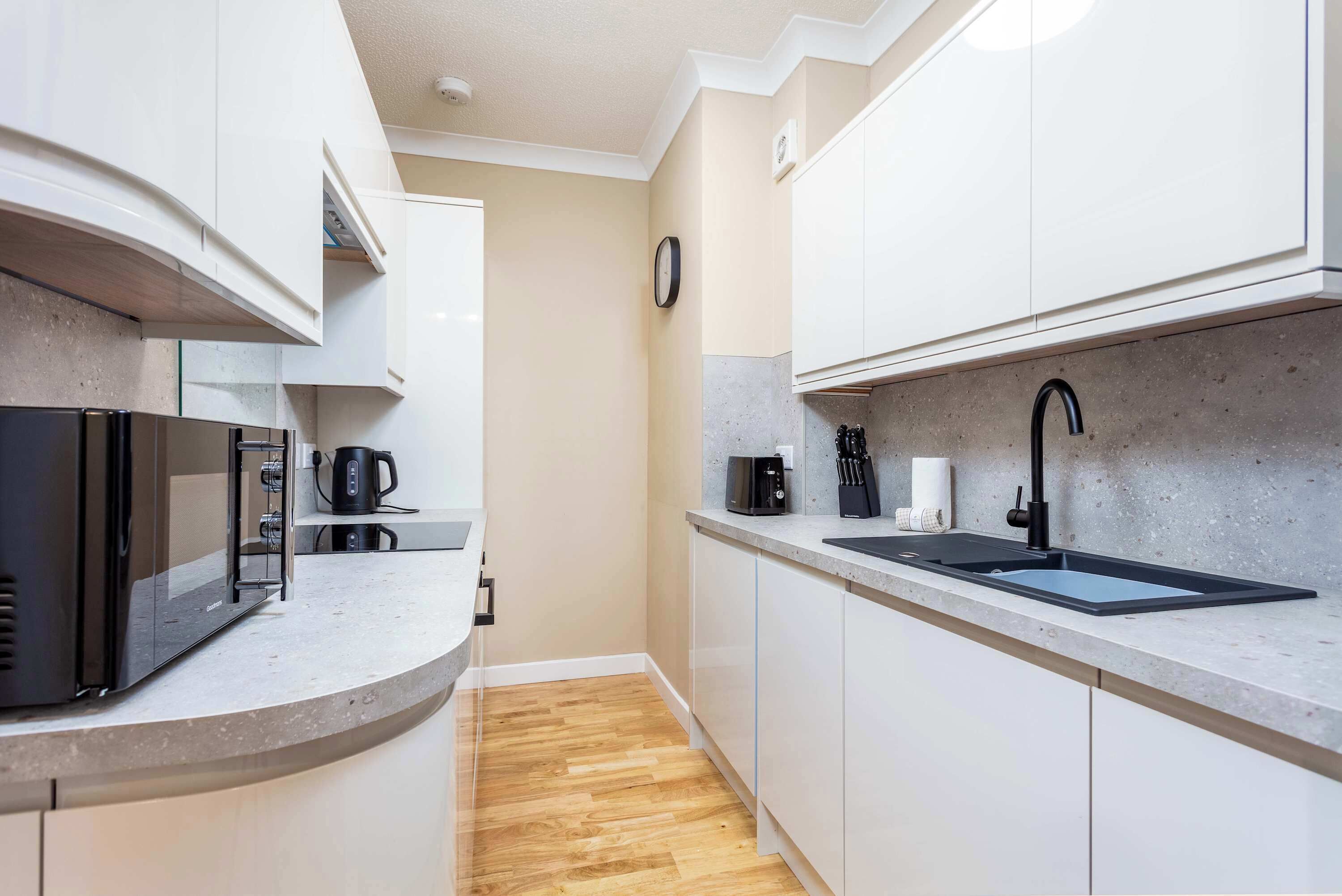 A modern kitchen with white cabinets, a black sink, a coffee maker, and a microwave.