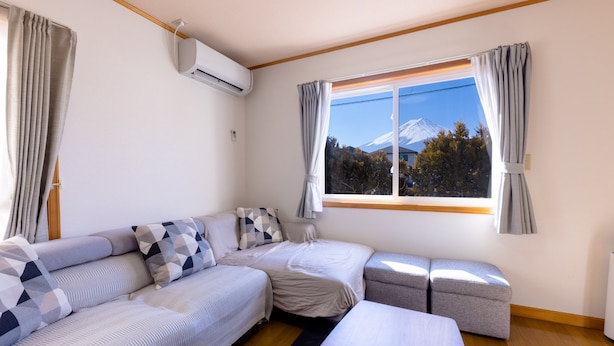 A room with a bed, a sofa, a window with a view of a mountain, and an air conditioning unit. - Ma Maison Mt. Fuji Kawaguchiko (Fujikawaguchiko)