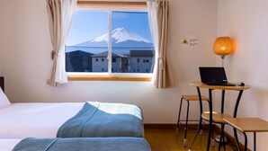 A hotel room with a bed, a desk with a laptop, a chair, a lamp, and a window with a view of a mountain. - Ma Maison Mt. Fuji Kawaguchiko (Fujikawaguchiko)