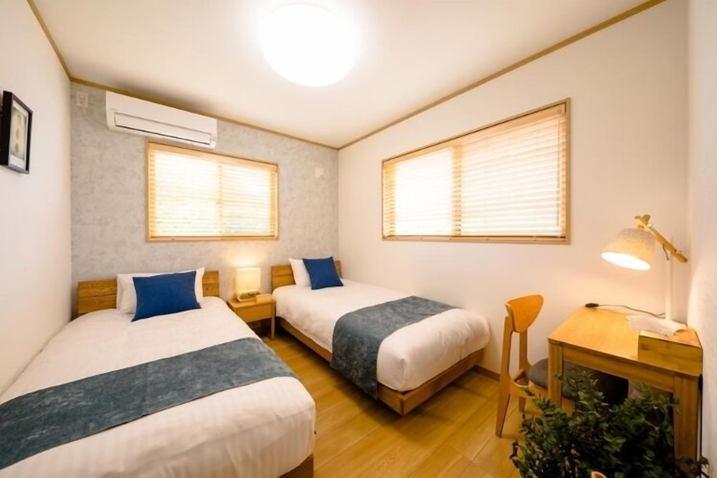 A room with two beds, a desk, a chair, and a lamp.