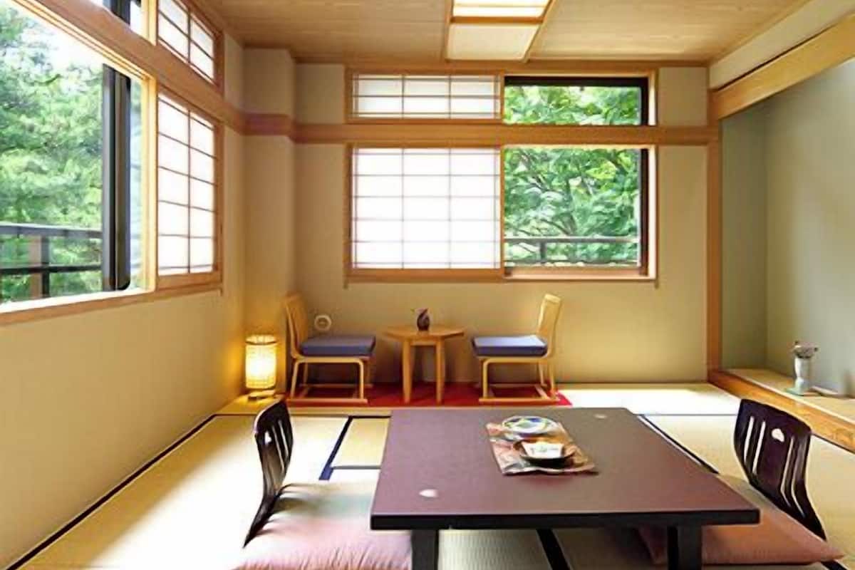 Una habitación tradicional con esteras tatami, una mesa baja, dos sillas y una mesita con una lámpara.