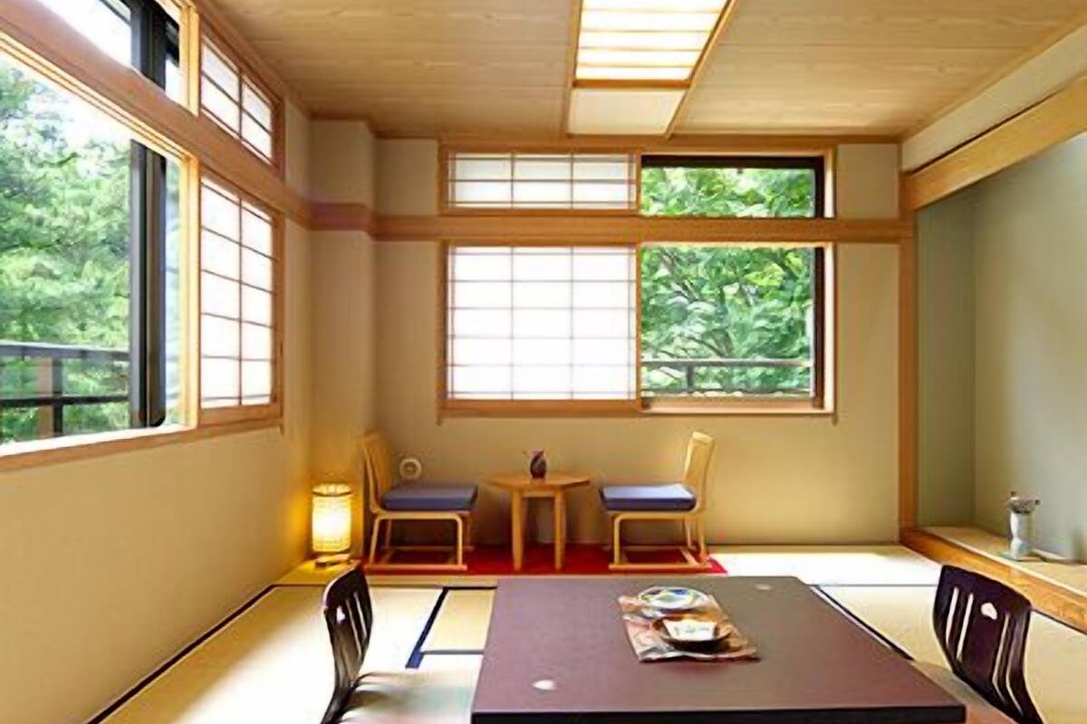 Una habitación tradicional japonesa con suelo de tatami, una mesa baja, dos sillas y ventanas grandes.