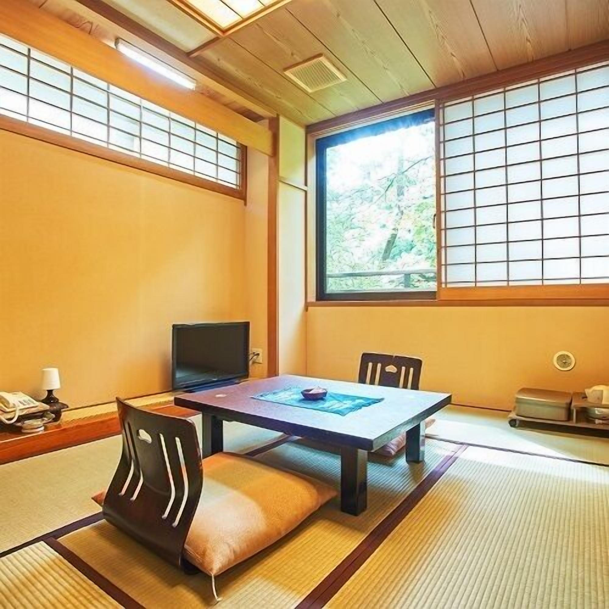 Una habitación japonesa tradicional con suelo de tatami, una mesa baja, un televisor y una ventana con vistas a árboles.