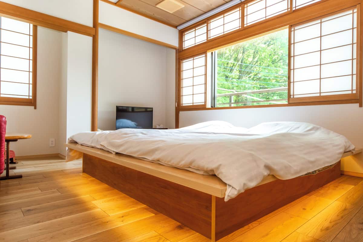 Una habitación con una cama de madera, ventanas amplias, un escritorio y un televisor.