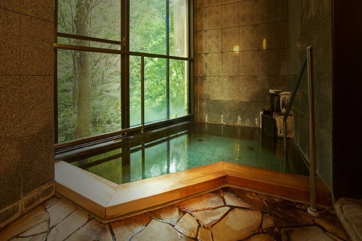 Una habitación con paredes de piedra, una bañera de hidromasaje con cristal y un banco de madera, sobre un suelo de piedra.