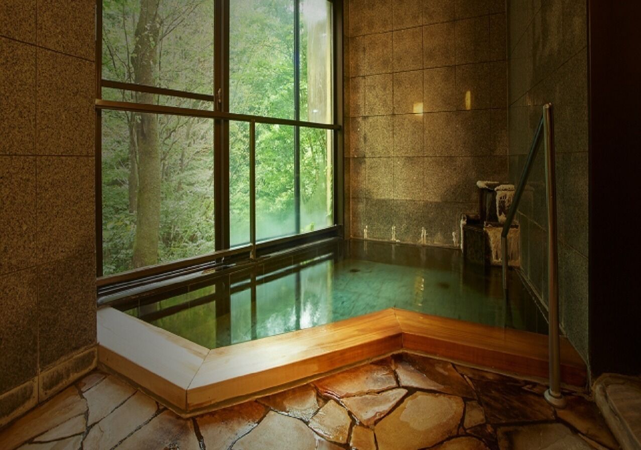 Una habitación con paredes de piedra, una bañera de hidromasaje con cristal y un banco de madera, sobre un suelo de piedra.