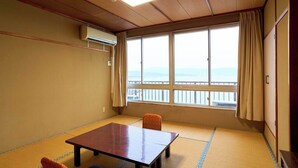 Une pièce avec un sol recouvert de tatamis, une table en bois, une chaise, une grande fenêtre donnant sur un beau paysage et un appareil de climatisation.