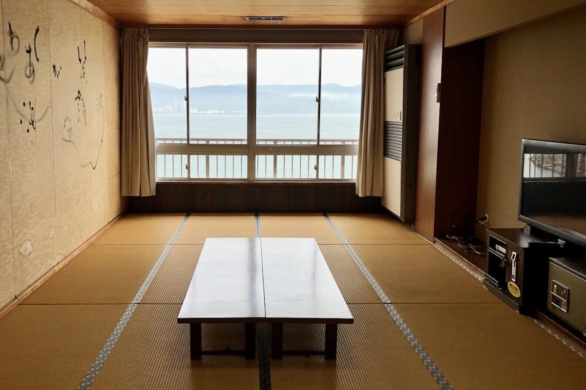Une pièce avec un sol recouvert de tatamis, une table, un téléviseur et une vue sur la mer.