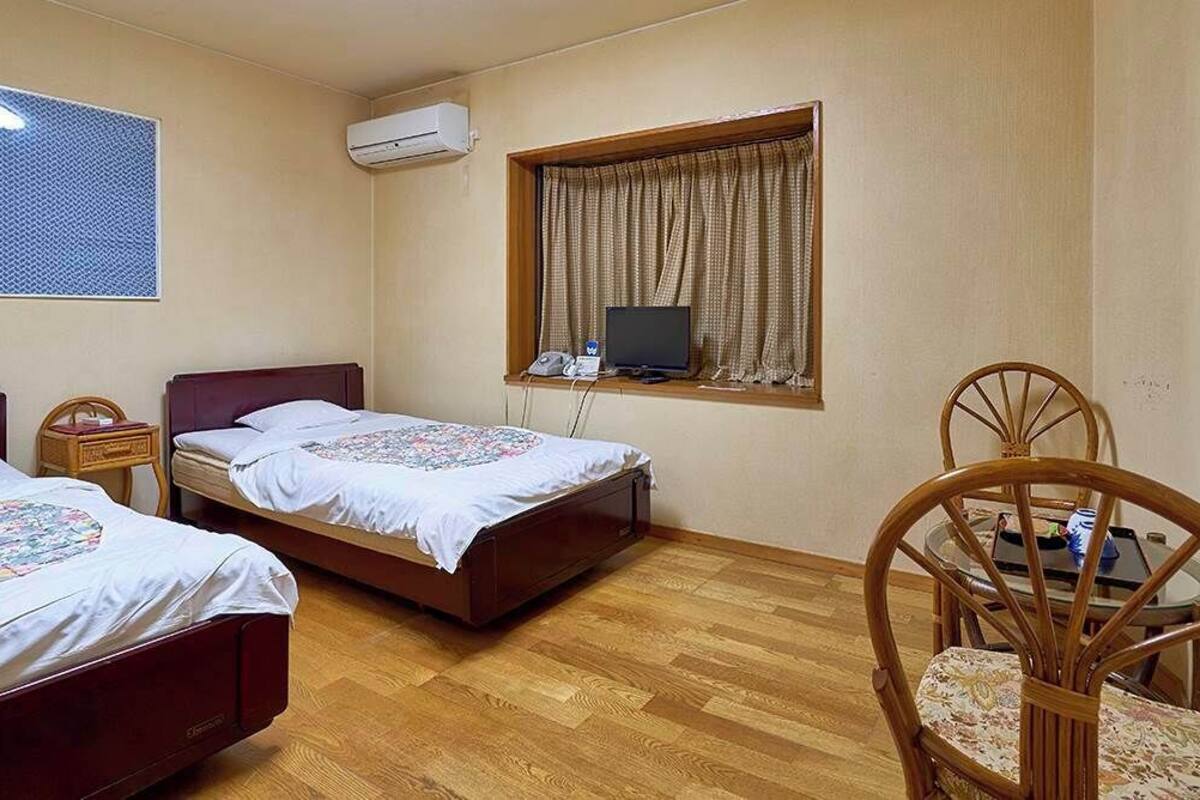 Une chambre d’hôtel avec deux lits, une télévision, une fenêtre avec des rideaux, une chaise et une petite table.