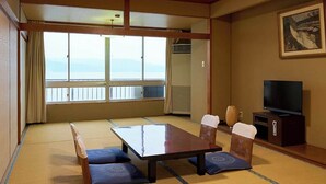 Une pièce de style japonais traditionnel, avec un sol recouvert de tatamis, une table basse, des coussins, un téléviseur et une grande fenêtre offrant une belle vue.