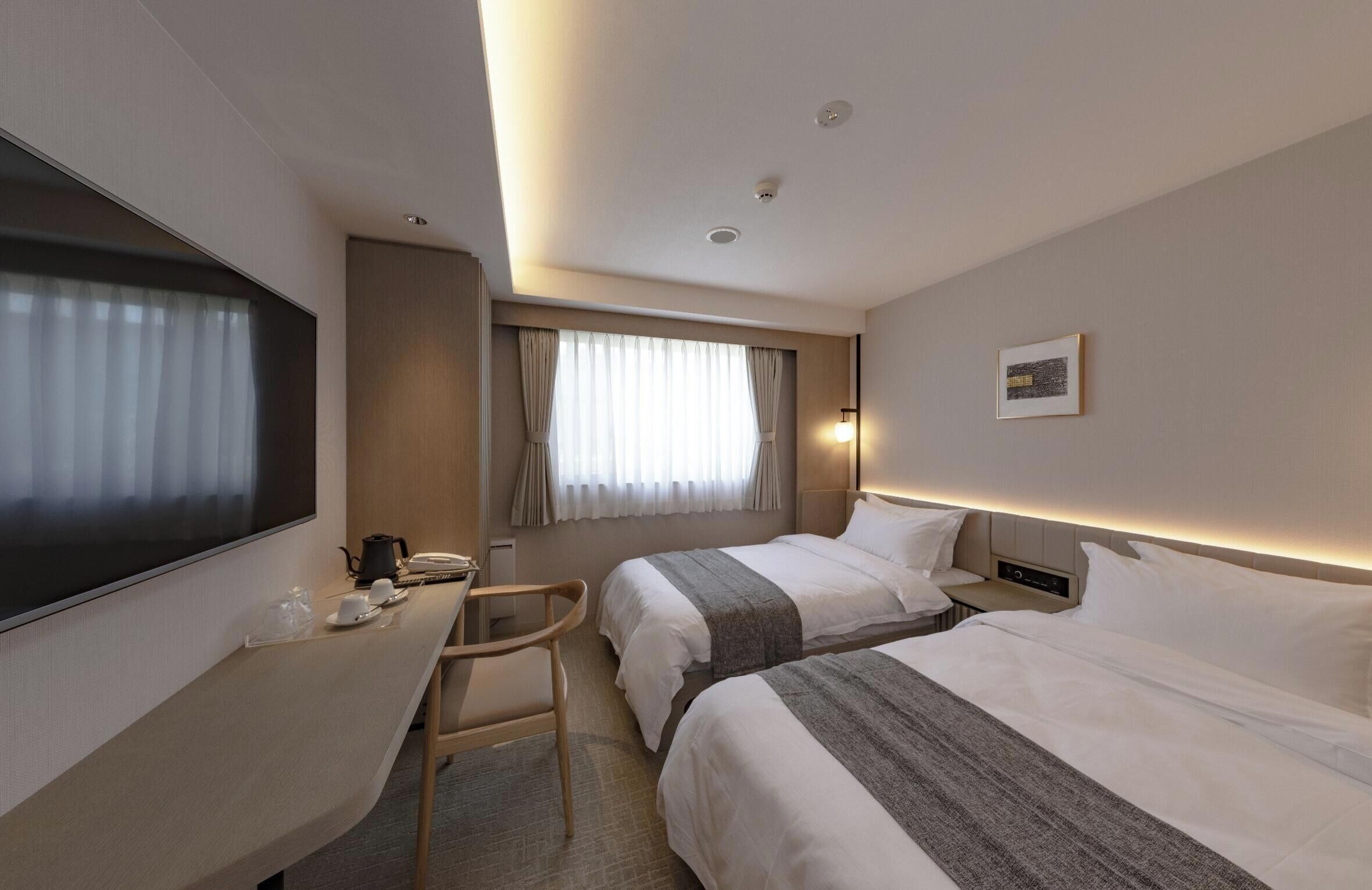 A hotel room with two beds, a desk, a chair, a TV, and a window with curtains.