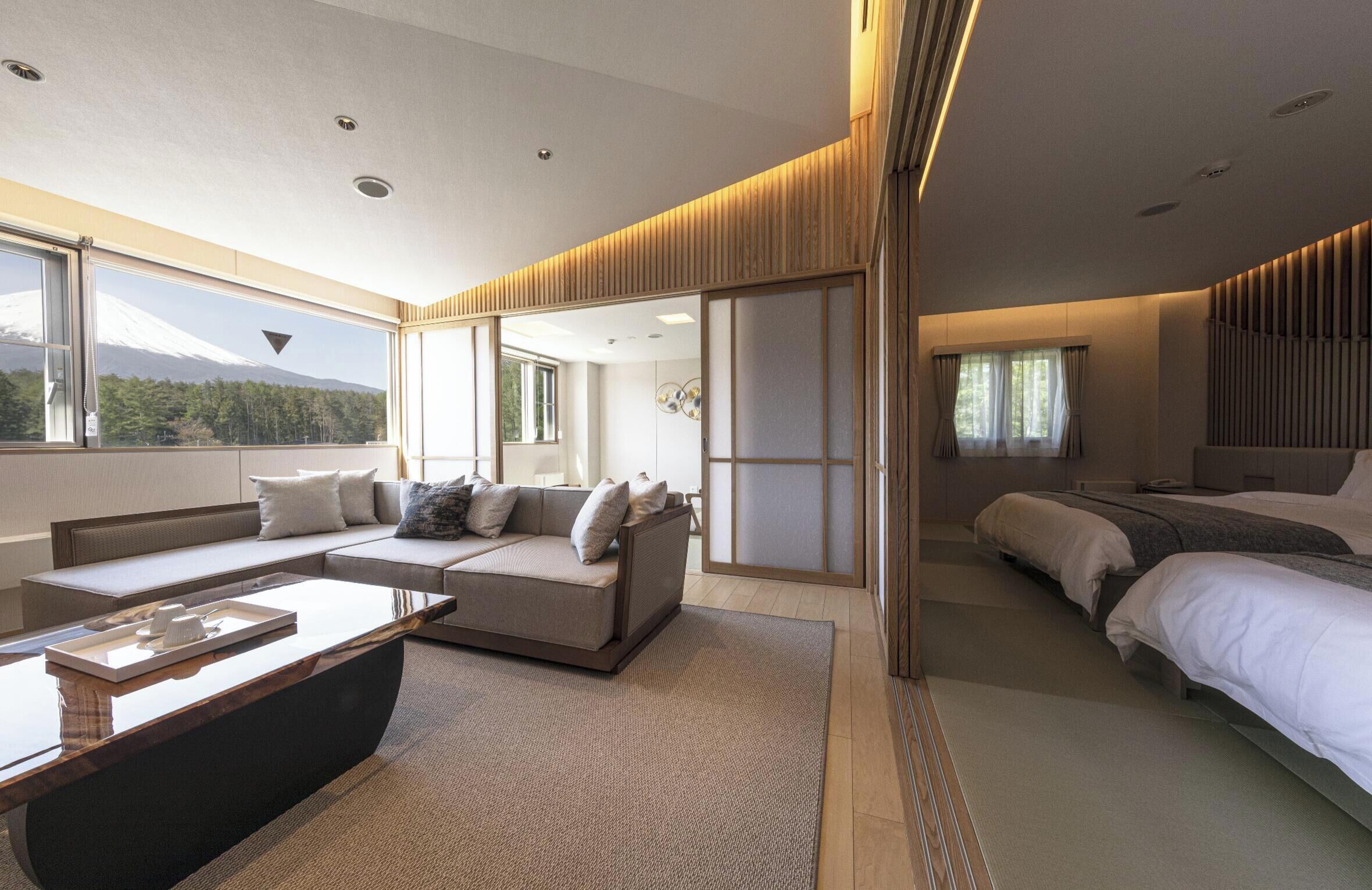 Une chambre d’hôtel moderne avec un canapé, un lit, une table de chevet et une vue sur une montagne.