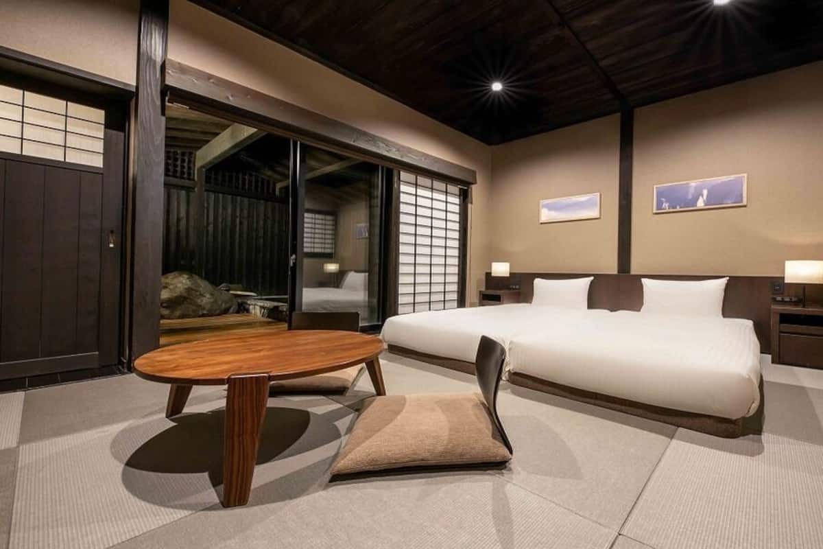 A traditional Japanese-style room with tatami flooring, a low wooden table, a sofa, and a bed with white bedding.