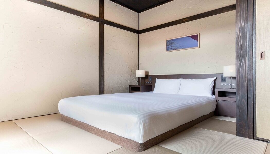 Une chambre d’hôtel avec un lit, des tables de chevet, une lampe et un tableau au mur.