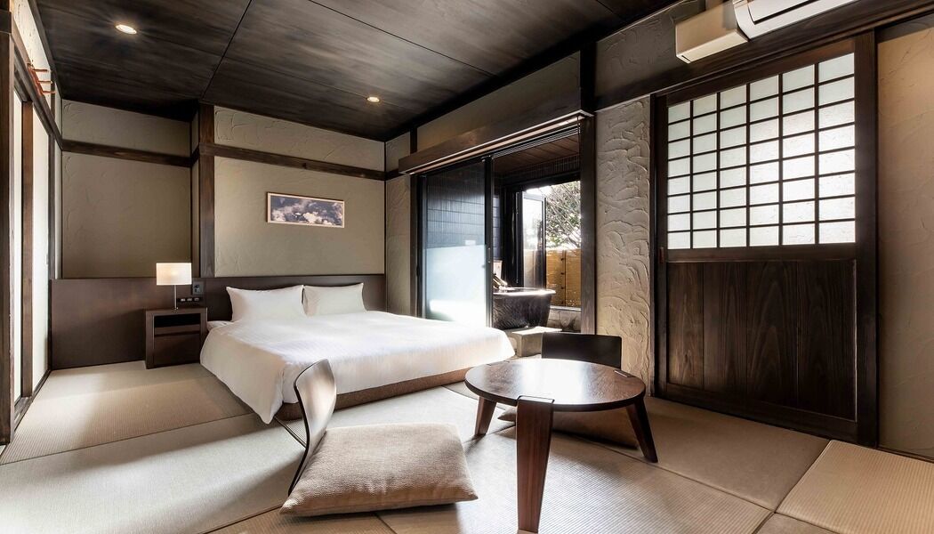 Une pièce de style japonais traditionnel, avec un sol recouvert de tatamis, un lit, une petite table et une fenêtre à carreaux.