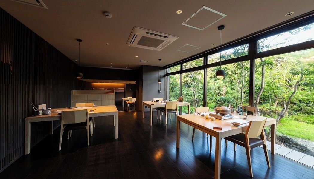 A modern kitchen with dark wood flooring, a dining area with a large window overlooking greenery, and a built-in kitchen counter.