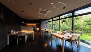 A modern kitchen with dark wood flooring, a dining area with a large window overlooking greenery, and a built-in kitchen counter. - Nagomi Tsuki (Beppu)