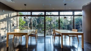 A modern dining area with a large table and chairs, large windows with a view of trees, and a ceiling with recessed lighting. - Nagomi Tsuki (Beppu)