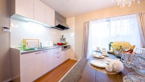 A modern kitchen with white cabinets, a stainless steel range hood, and a dining area with a table set for four. - Villa Hanasaku Fujikawaguchiko A (Fujikawaguchiko)