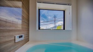 A modern bathroom with a bathtub, a window, and a thermostat on the wall. - Villa Hanasaku Fujikawaguchiko A (Fujikawaguchiko)