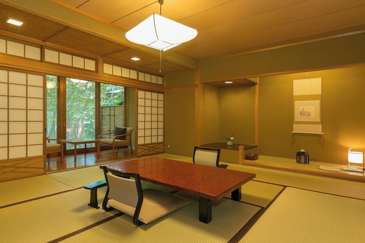 Una habitación japonesa tradicional con suelo de tatami, una mesa baja, sillas, una puerta corredera y un colgador con luz.