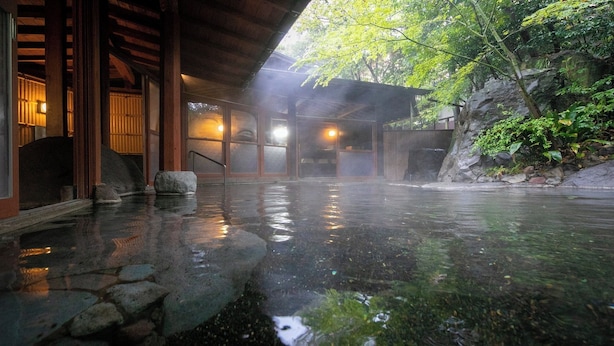 A traditional Japanese onsen with stone-tiled floors, wooden structures, and a natural rock backdrop. - Yufuin Onsen Hinoharu Ryokan (Yufu)