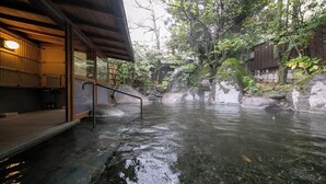 A traditional Japanese onsen with a wooden building, a stone pathway, and a natural rock formation. - Yufuin Onsen Hinoharu Ryokan (Yufu)