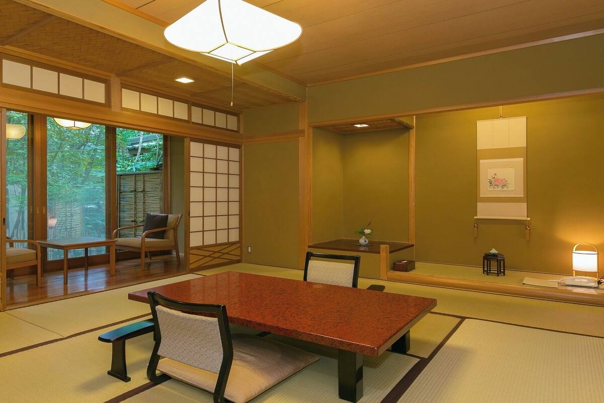 Una habitación japonesa tradicional con suelo de tatami, una mesa baja, sillas, una lámpara colgante y puertas correderas.