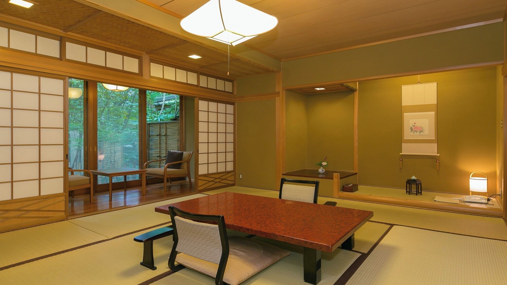 Una habitación japonesa tradicional con suelo de tatami, una mesa baja, sillas, una lámpara colgante y puertas correderas.