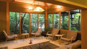 A room with large windows, wicker furniture, a wooden table, and a ceiling light fixture. - Yufuin Onsen Hinoharu Ryokan (Yufu)