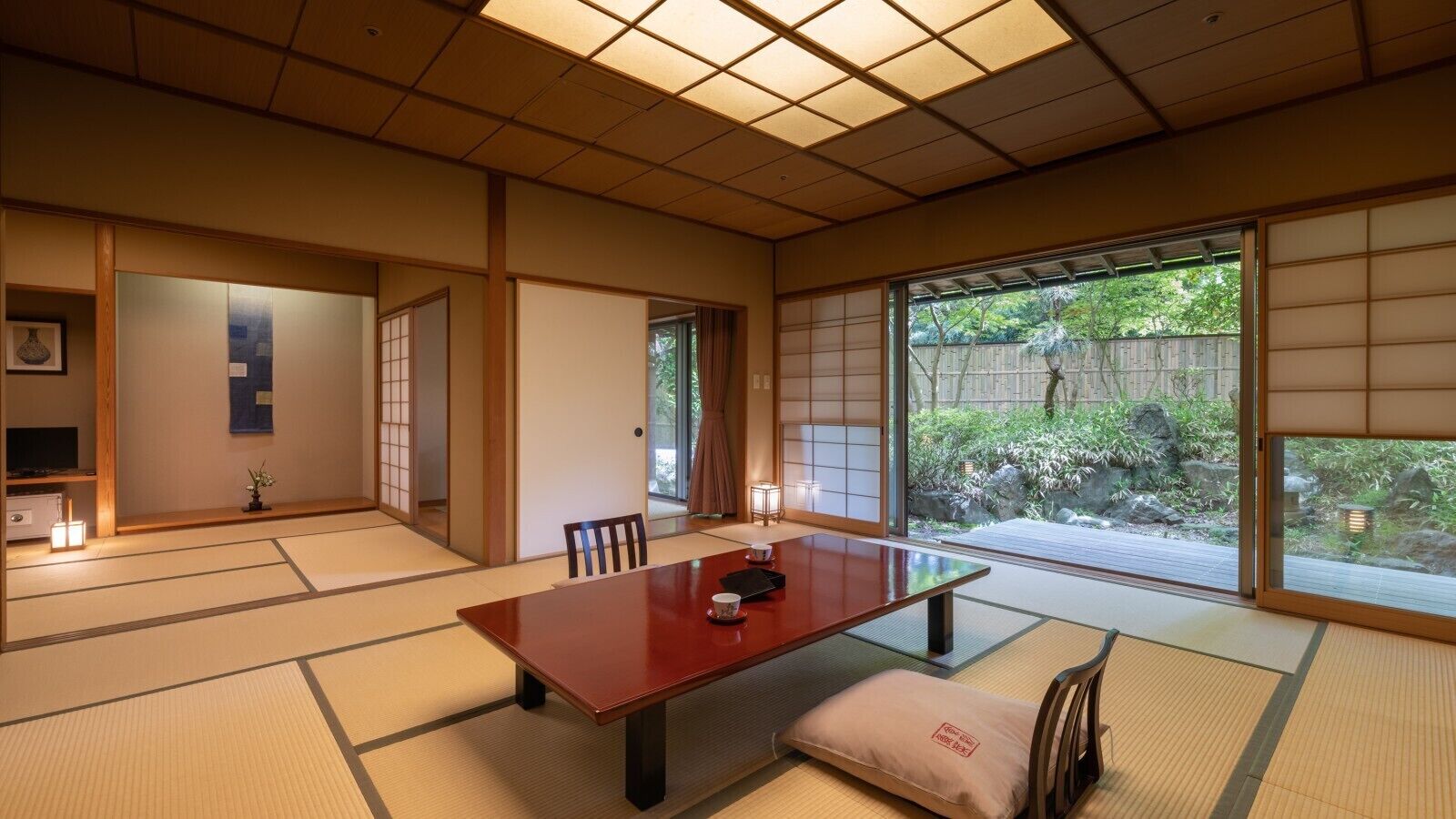 A traditional Japanese room with tatami flooring, a low table, sliding doors, and a view of a garden.
