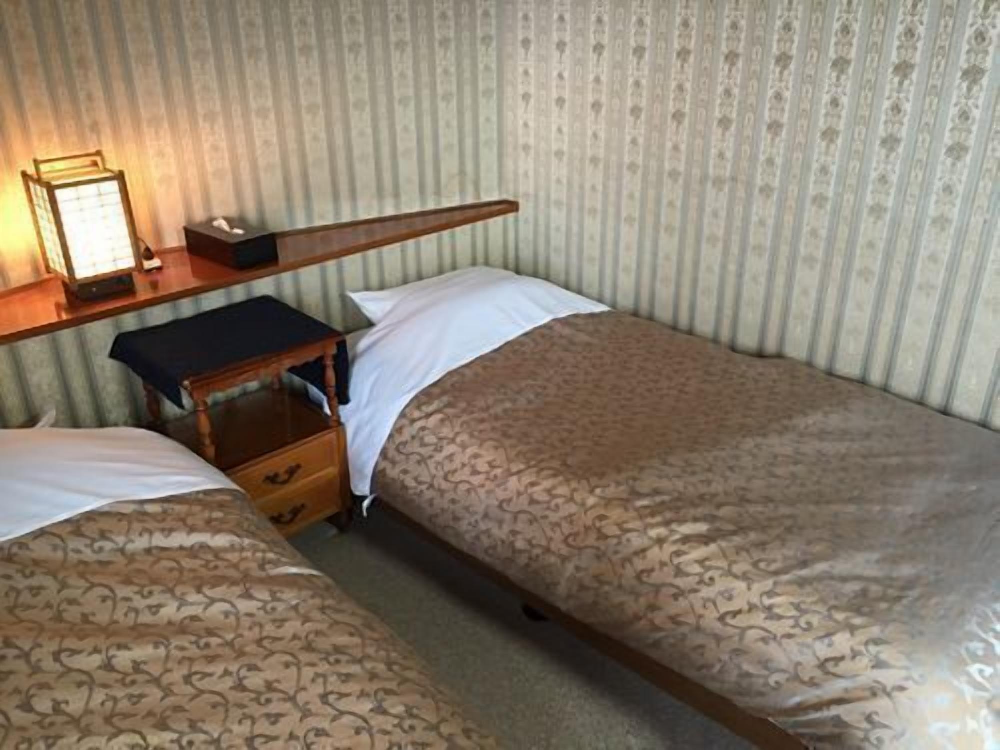 Un lit simple avec une couvre-lit à motifs, une table de chevet avec une lampe et une petite commode.