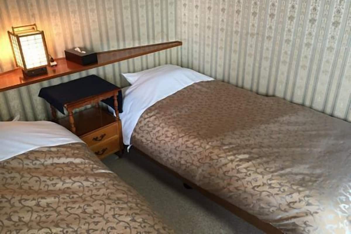 Un lit simple avec une couvre-lit à motifs, une table de chevet avec une lampe et une petite commode.