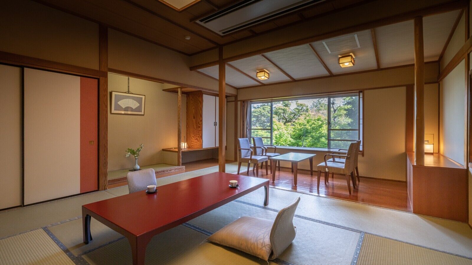A traditional Japanese-style room with tatami flooring, a low wooden table, and a view of greenery outside.