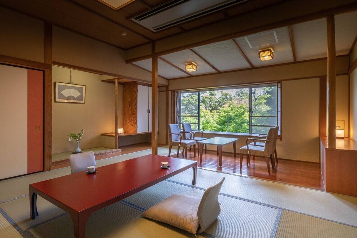 Ein traditioneller japanischer Raum mit Tatami-Böden, einem niedrigen Holztisch und Blick auf Grünflächen.