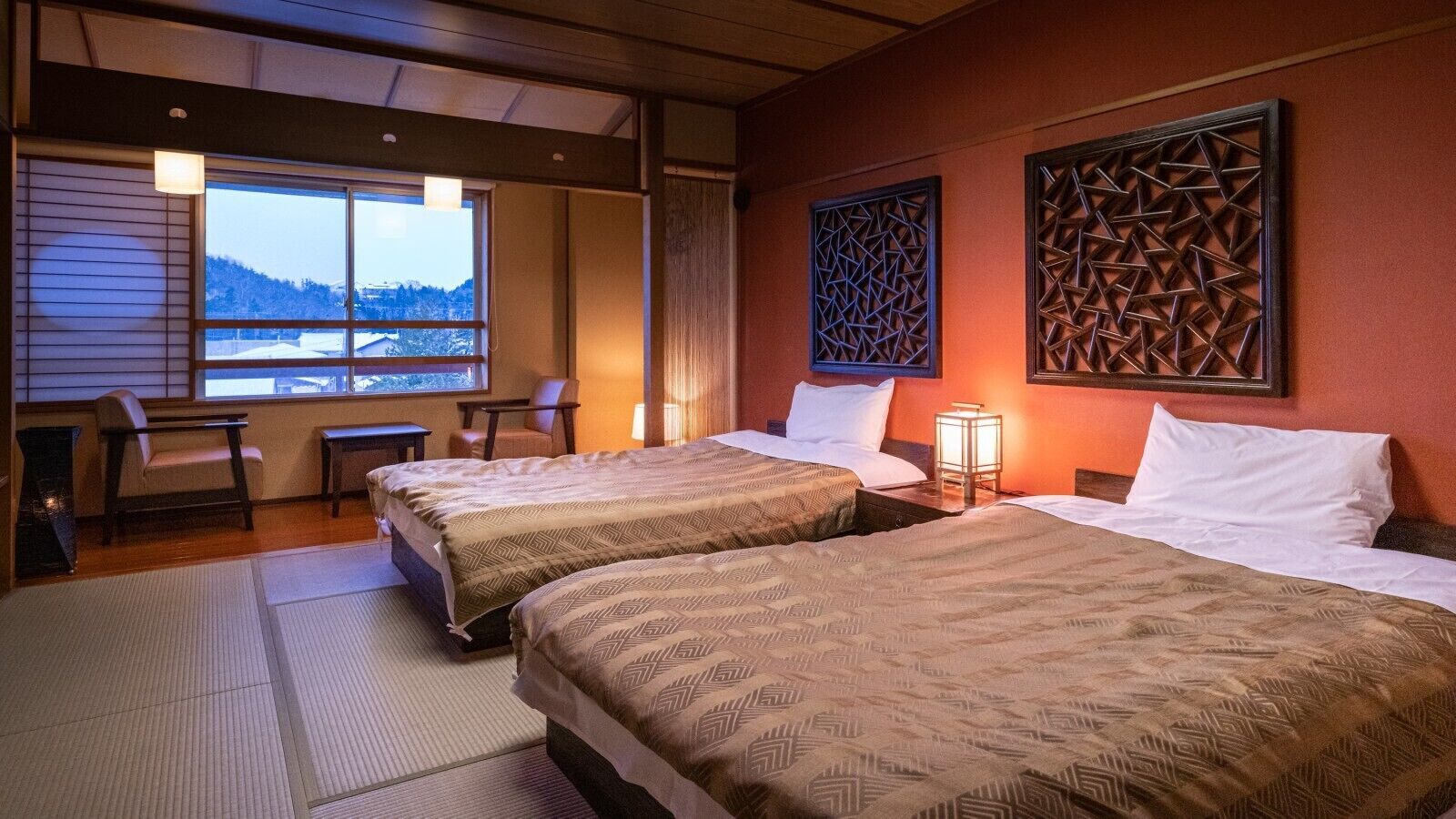 A hotel room with two beds, a sitting area with a chair and table, and a window with a view of a snowy landscape.