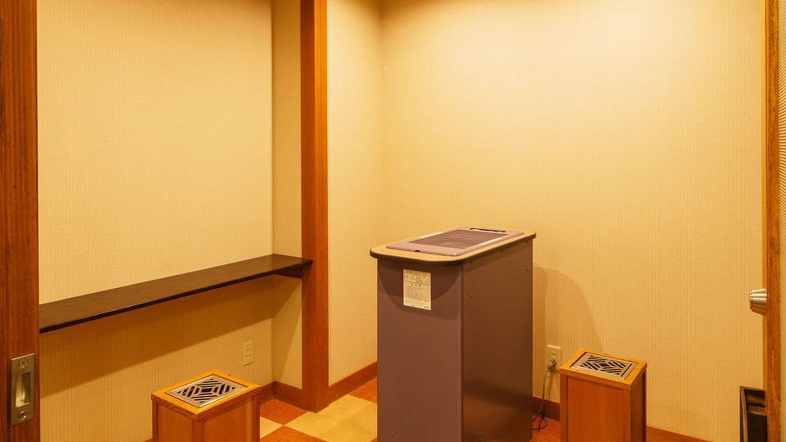 A narrow hallway with a wooden door frame, a small trash bin, and a wall-mounted intercom.