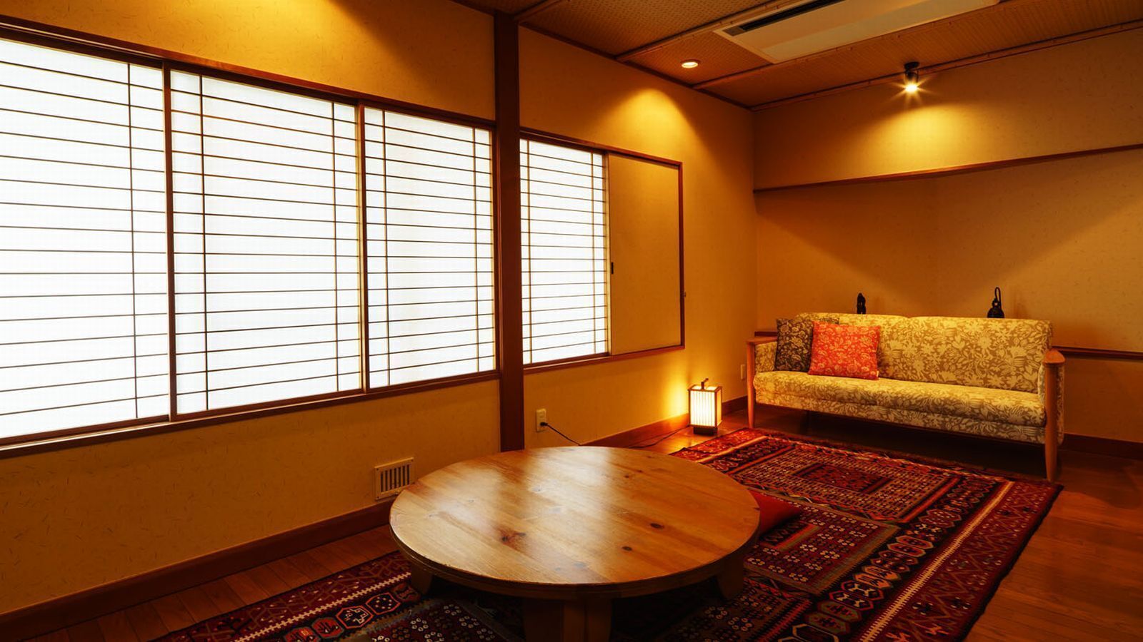 Une pièce de style japonais traditionnel, avec un sol recouvert de tatamis, une table basse, un canapé avec des coussins et des paravents en papier de riz (shoji).
