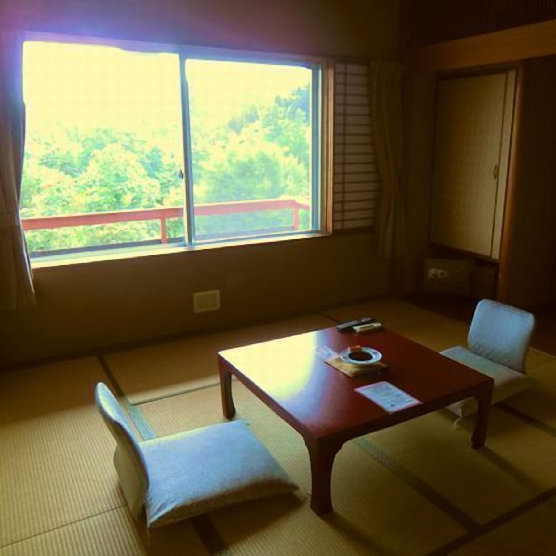 A room with tatami flooring, a low table, a chair, and a view of greenery through a window.