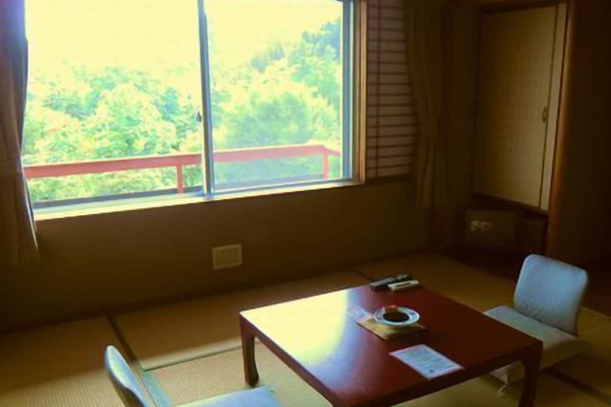 A room with tatami flooring, a low table, a chair, and a view of greenery through a window.