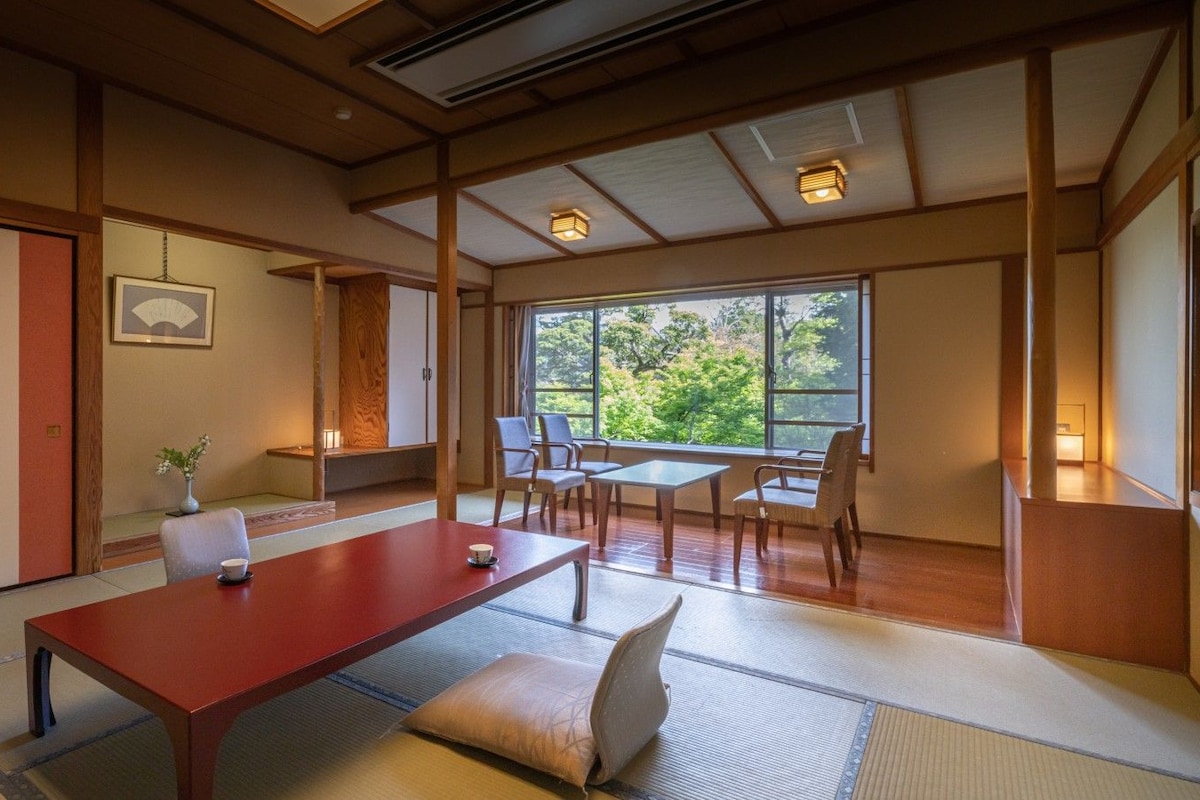 Une pièce de style japonais traditionnel, avec un sol recouvert de tatamis, une petite table en bois et une vue sur la verdure environnante.
