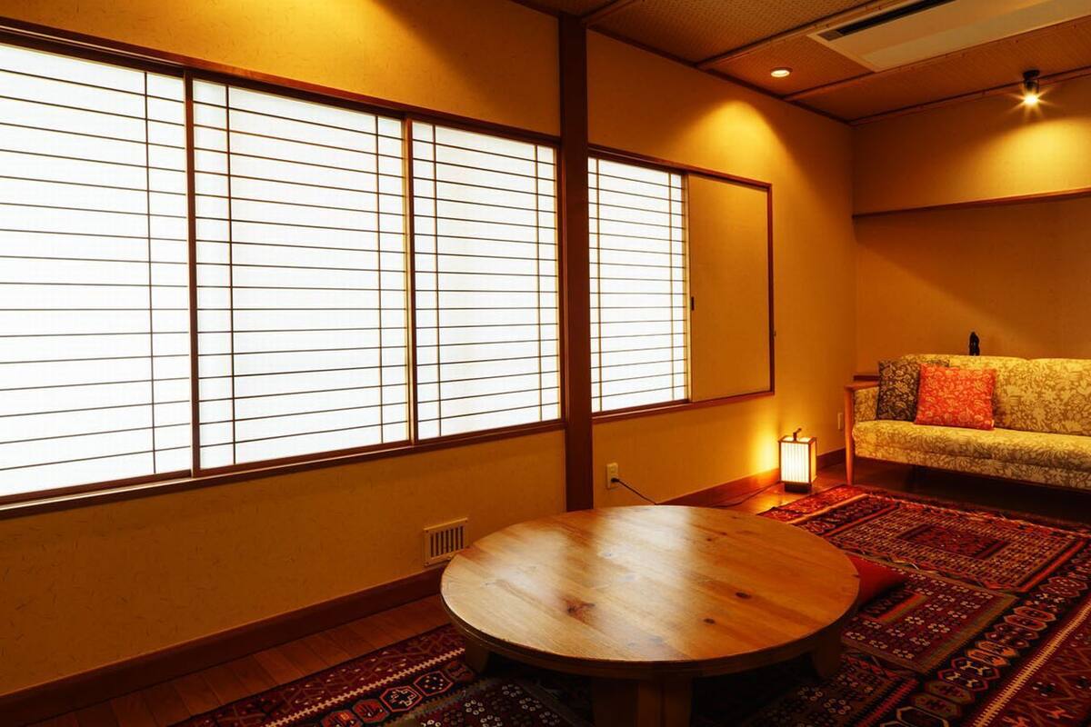 Ein traditioneller japanischer Raum mit Tatami-Bodenbelag, einem runden Holztisch, einer Couch mit Kissen und Shoji-Schirmwänden.